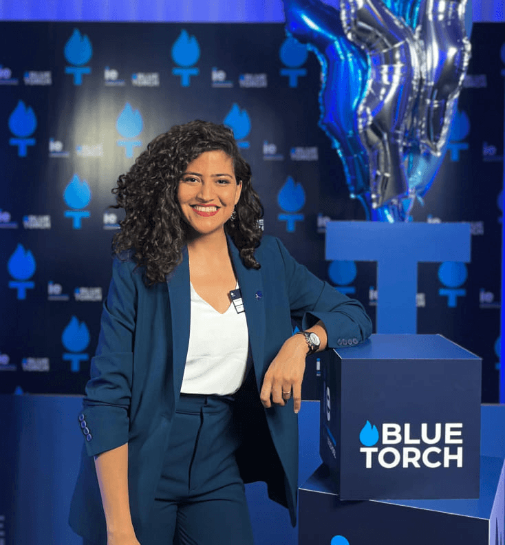 A woman in a blue suit is smiling while standing at a podium with the 'Blue Torch' logo.